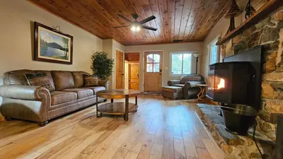 a living room with a couch and a stone fireplace at Knotty Pine Cabin with Artisan Stone Patio - Walk to Bass Lake in Bass Lake