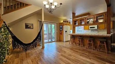 a living room with a kitchen and a bar with stools at Knotty Pine Cabin with Artisan Stone Patio - Walk to Bass Lake in Bass Lake