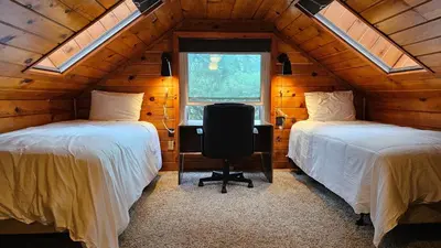 two beds in a room with a desk and a window at Knotty Pine Cabin with Artisan Stone Patio - Walk to Bass Lake in Bass Lake