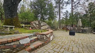 a brick patio with a table and chairs and an umbrella at Knotty Pine Cabin with Artisan Stone Patio - Walk to Bass Lake in Bass Lake