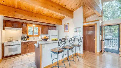 a kitchen with wooden cabinets and a counter with stools at Lake Beach Access Pool Tennis Walk to Chambers Tahoe Timber by AvantStay in Homewood