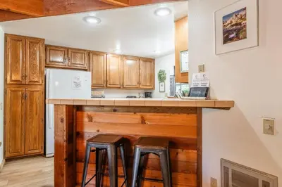 a kitchen with wooden cabinets and a counter with stools at Snowflower #79 - Updated 2 Bedroom & Loft, 3 Bath, Sleeps 8, Steps away from Free Town Shuttle in Mammoth Lakes