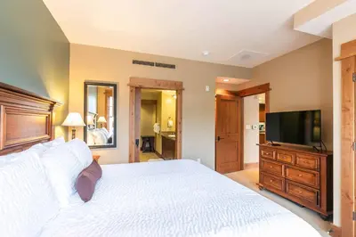 a bedroom with a white bed and a flat screen tv at Catamount Lodge 201B by East West Hospitality in Truckee