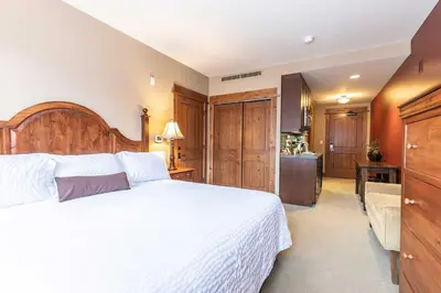 a bedroom with a large white bed and a kitchen at Catamount Lodge 201A by East West Hospitality in Truckee