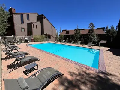 a swimming pool with chaises and chairs next to a house at Walk-to-Lifts Condo with Hot Tub, Dog Friendly in Mammoth Lakes