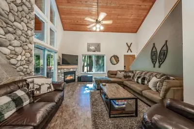 a living room with couches and a stone wall at Cabin at the Creek Family Fun Starts Here! in Shaver Lake