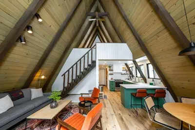 a living room and kitchen of a house with wooden ceilings at Dogwood Peak Mid-Century A-Frame with AC Style in Shaver Lake