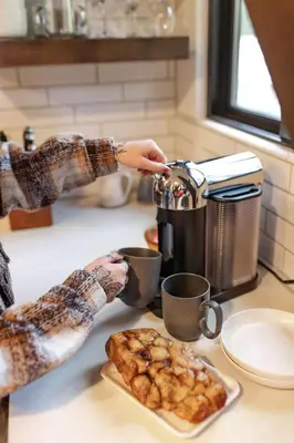 a person is holding cups of coffee on a counter at Dogwood Peak Mid-Century A-Frame with AC Style in Shaver Lake