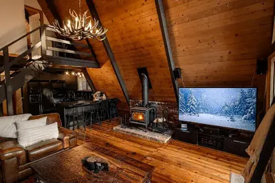 a living room with a large screen tv and a couch at Modern Black A-Frame overlooking a Meadow w AC! in Shaver Lake