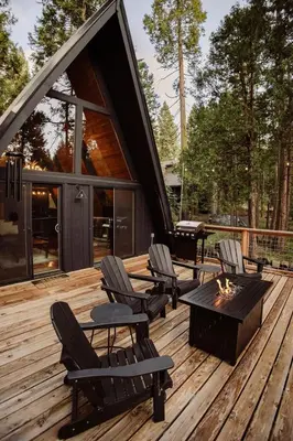 a deck with chairs and a fire pit on a cabin at Modern Black A-Frame overlooking a Meadow w AC! in Shaver Lake