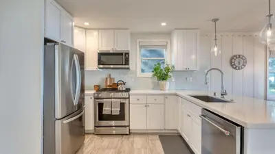a kitchen with white cabinets and a stainless steel refrigerator at West Shore Lake House by AvantStay Ski Cabin w Backyard Sledding Hill in Homewood