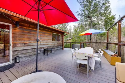 a deck with a red umbrella and tables and chairs at Peaceful Wooden Cabin, 2 Mi to Bass Lake! in Oakhurst