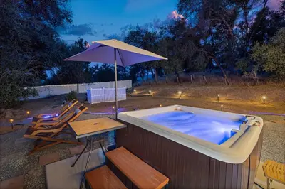 a hot tub with an umbrella and a table and chairs at HIlltop Oasis with games, hot tub, Fire-pit, Deck, Views in Oakhurst