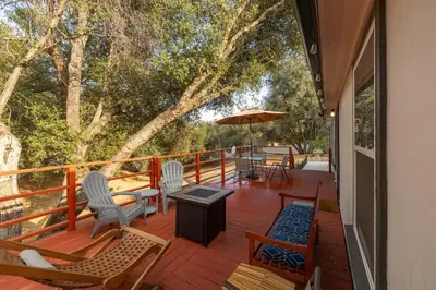 a deck with chairs and tables and an umbrella at HIlltop Oasis with games, hot tub, Fire-pit, Deck, Views in Oakhurst