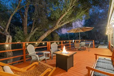 a wooden deck with chairs and an umbrella and a table at HIlltop Oasis with games, hot tub, Fire-pit, Deck, Views in Oakhurst