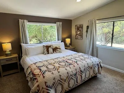 a bedroom with a large bed with two windows at Manzanita Hideaway Hot Tub Sunset views Yosemite in Ahwahnee
