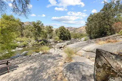 a bench sitting on the side of a river at 10 Min Drive to the Sequoias in Three Rivers