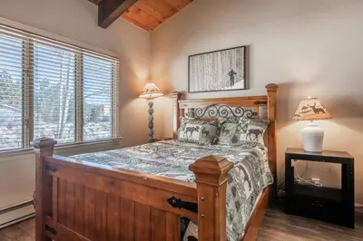 a bedroom with a wooden bed in a room with windows at Mammoth TwnHm hot tub walk to town in Mammoth Lakes