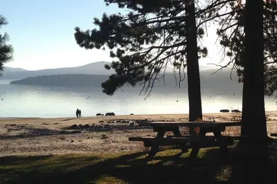 a picnic bench sitting on a beach near a lake at Happy Cabin Near Snow and Lake with Hot Tub, Dogs OK in Tahoe Vista
