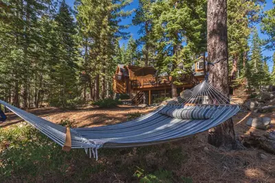 a hammock in front of a house in the woods at Home for 10 Private Hot-Tub Close to Ski Private Beach Access w Double Decker pier Book on Mobile for Promo Price in Carnelian Bay