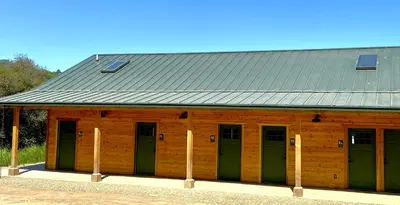 a wooden building with green doors and a metal roof at Wildhaven Yosemite Glamping in Mariposa