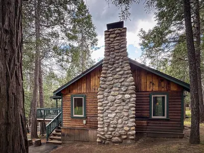 a log cabin with a stone chimney in the woods at 10 Little Cabin In The Woods in North Wawona