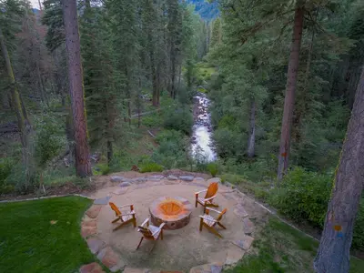 a patio with a table and chairs next to a river at Eagle Rock By Tahoe Getaways - 4BR West Shore w Hot Tub & Close to Hiking! in Homewood