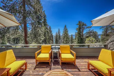 a deck with yellow chairs and tables and trees at Sky Rocks - Private Beach, Buoy & Pier, HOA Swimming Pool & Tennis in Kings Beach