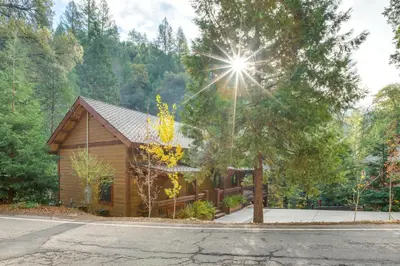 a log cabin in the woods with the sun shining at Bear Lodge Waterfront Cabin with Level 2 EV Charger in Sutter Creek