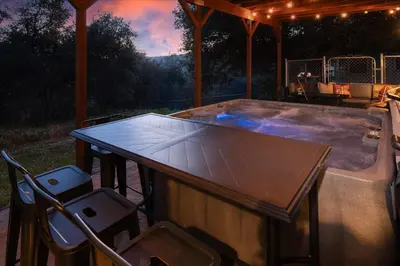 a hot tub on a patio with a table and chairs at Sequoia's Dream with Mountain View, Spa, Heated Floor, Bar, Cinema! in Oakhurst