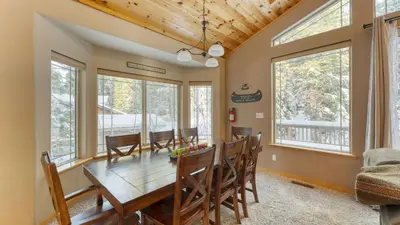 a dining room with a wooden table and chairs and windows at Cherry Hills Spacious Tahoe Cabin with Deck Fireplace Open Interiors in South Lake Tahoe
