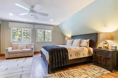 a bedroom with a bed and a chair and windows at Tahoe Dreamer by Tahoe Getaways - Pet Friendly 4 BR Gated Home w Fenced Yard, Game Room & Walk to Lake! in Carnelian Bay