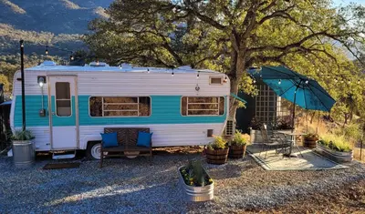 a blue and white trailer with a table and an umbrella at Cozy Farm Stay for Two in Three Rivers