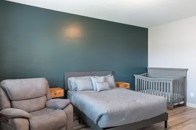 a bedroom with a bed and a chair and a crib at Spacious 4BR Home With BBQ, Near Sequoia & Fresno in Hanford
