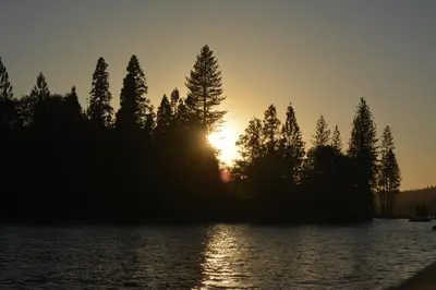 a sunset on a island in the water with trees at SunRidge at Willow Cove Free Night Special in Bass Lake