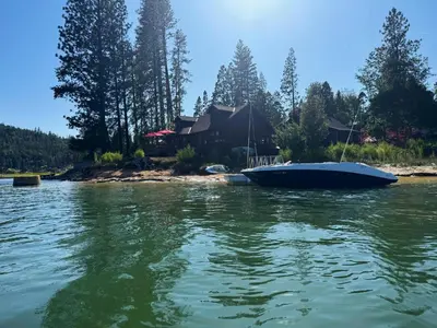 a boat on the water in front of a house at Wishon Lake Front, Price Reduced, 3day Min in Bass Lake