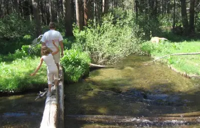 a man and a child crossing a bridge over a creek at Plush Mammoth Condo w Balcony Views in Mammoth Lakes