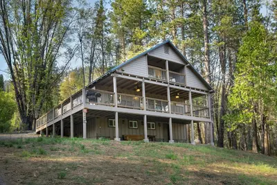 a large house with a wrap around porch in the woods at Hilltop Haven in Wawona