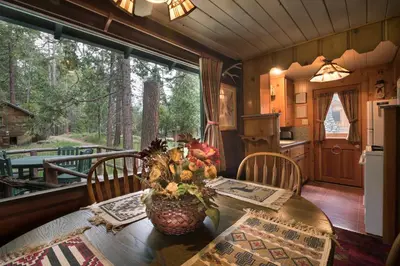 a dining room with a table and a kitchen with a window at Chipmunk Hollow in Wawona