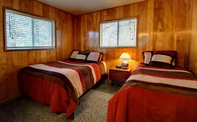 two beds in a room with wooden walls and windows at Longview at The Redwoods in Wawona