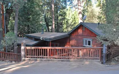 a log cabin with a fence in the woods at The Tree House in Wawona