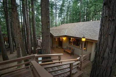 a small cabin in the woods with a wooden deck at We-Dunn-It in Wawona