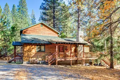 a log cabin with a large deck in the woods at River Refuge in Wawona