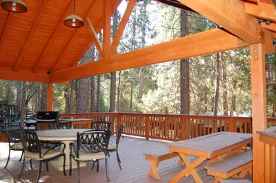 a wooden deck with tables and chairs in the woods at Deer Den in Wawona