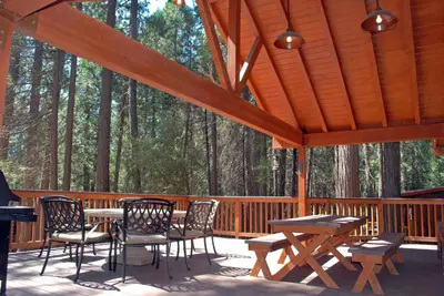 a wooden deck with tables and chairs and trees at Deer Den in Wawona