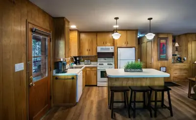 a kitchen with wooden cabinets and a island with bar stools at Pine Creek Cabin in Wawona