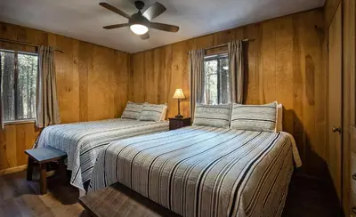 two beds in a room with wooden walls and windows at Pine Creek Cabin in Wawona