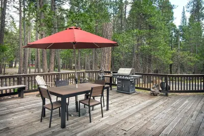 a table and chairs with an umbrella on a deck with a grill at Rosenberg's Creekside Cabin in Wawona
