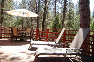 a deck with chairs and a table and an umbrella at Manzanita Lodge in Wawona