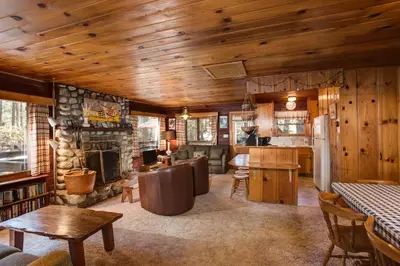 a living room with a fireplace and wooden ceilings at Creekside Cabin in Wawona